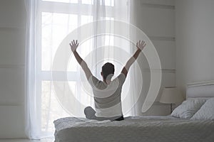 Happy young man stretching in bed after waking up, back view