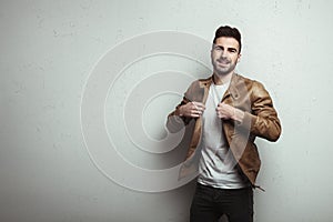 Happy young man with stubble wearing leather jacket and t-shirt, white grunge wall with cracks background