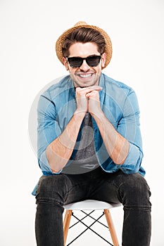 Happy young man in sunglasses sitting on chair and smiling