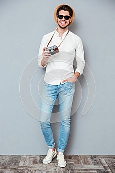 Happy young man in sunglasses standing and holding vintage camera