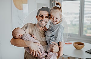Happy young man taking care of his newborn baby and little daughter indoors at home, paternity leave