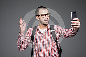 Happy young man taking self portrait photography through phone over gray background.