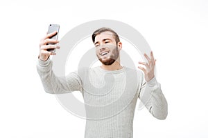 Happy young man taking selfie and showing why gesture over white background