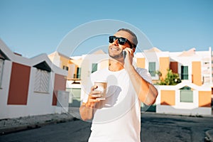 Happy young man talk on phone and drink coffee and walk on street