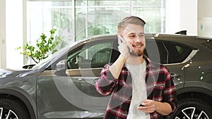 Happy young man talking on the phone after buying a new car at the dealrrship