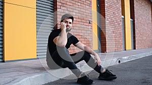 Happy young man talking on the phone enthusiastically while sitting on the sidewalk in the middle of the city.