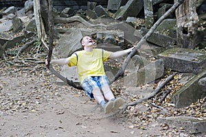 Happy young man, the teenager, the tourist, shakes on a liana as on a swing on Beng Mealea temple ruin in the Koh Ker complex, Si