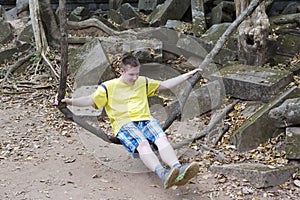 Happy young man, the teenager, the tourist, shakes on a liana as on a swing on Beng Mealea temple ruin in the Koh Ker complex, Si