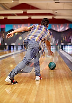 Happy young man throwing ball in bowling club