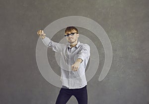 Happy young man in thug life glasses dancing gangnam style isolated on grey background