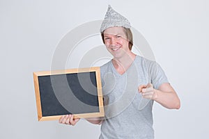 Happy young man with tin foil hat holding blackboard and pointing at camera