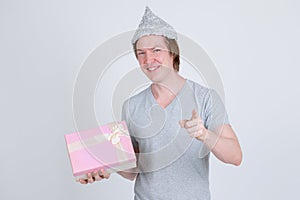 Happy young man with tin foil hat holding gift box and pointing at camera
