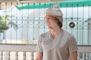 Happy young man with tin foil hat thinking as conspiracy theory concept outdoors