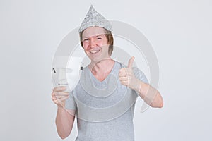 Happy young man with tinfoil hat holding white mask and giving thumbs up