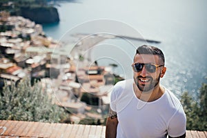 Happy young man traveler smiling at italian coast view.Man traveling to European south coast.Enoying sunny weather medditerranean