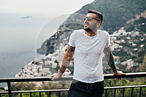 Happy young man traveler smiling at italian coast view.Man traveling to European south coast.Enoying sunny weather medditerranean