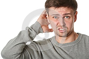 Happy young man with uncertain puzzled expression, on gray background photo