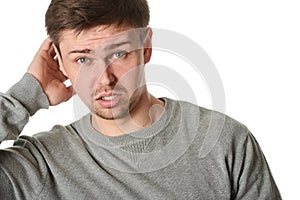 Happy young man with uncertain puzzled expression, on gray background