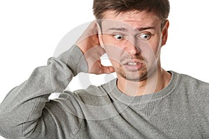 Happy young man with uncertain puzzled expression, on gray background