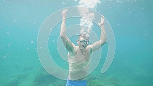 Happy young man underwater waves hands smiles and looks at camera on vacation.