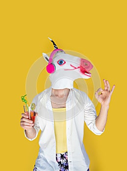 happy young man in unicorn mask and headphones with juice cocktail dancing over yellow background.