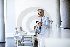 Happy young man using his mobile phone and smiling while his colleagues working in the background