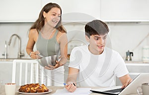 Happy young man using laptop in the kitchen while communicating with his girlfriend