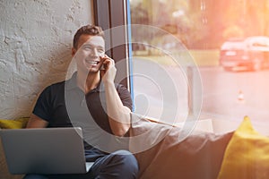 Happy young man using laptop and mobile phone on couch