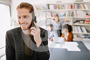 Happy young man using mobile phone and smiling while his colleagues working in office