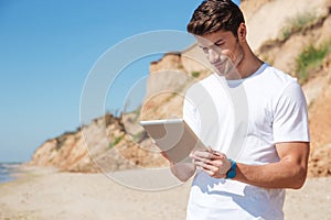 Happy young man using tablet on the beach