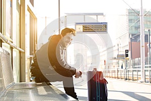 Happy young man waiting for train at station with bag