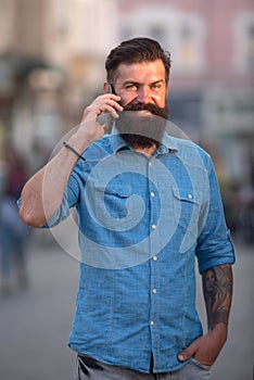 Happy young man walking on the street while talking by mobile phone.