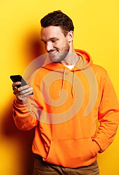 Happy young man wearing casual typing sms on yellow background