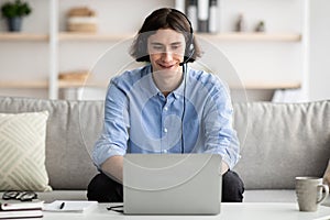 Happy young man wearing headphones, having online meeting on laptop or participating in webinar, working from home