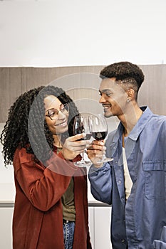 Happy young man and woman drinking with glasses in home. Cheering diverse couple toasting with wine in kitchen.