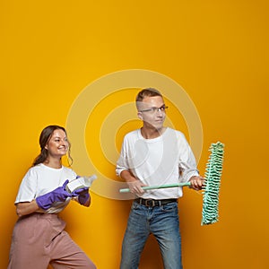 Happy young man and woman on orange studio background, cleaning service concept