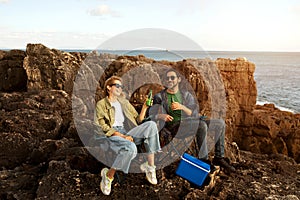 Happy Young Man And Woman Relaxing On Rocks Near Ocean Shore