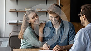 Happy young married couple buying house, signing property purchase contract