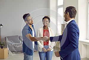 Happy young married couple buys house and closes deal with realtor with handshake.