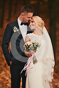 Happy young married couple in golden yellow fall autumn park. beautiful bride and stylish groom hugging in wedding day
