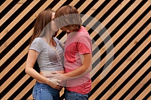Happy young married couple, husband hugs a beautiful adult pregnant wife. Stand against the background of a striped wall.