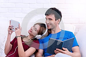 Happy married couple relaxing together at home with the wife lying back against her husband as she listen to music on tablet