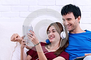 Happy married couple relaxing together at home with the wife lying back against her husband as she listen to music on tablet