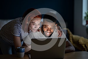 Happy young married multiracial couple using laptop together at home, planning summer vacation