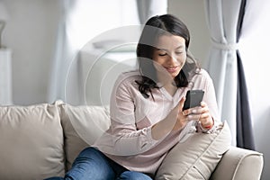 Happy young millennial woman with smartphone relaxing on couch