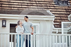 Happy young mixed race couple standing on the balcony at their new home. Hispanic couple looking into each others eyes