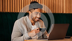 .. Happy young mixed race man sitting at a table in a cafe drinking coffee and using a laptop alone. One hispanic
