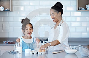 Happy young mixed race mother enjoying baking with her little daughter in the kitchen at home. Little hispanic girl