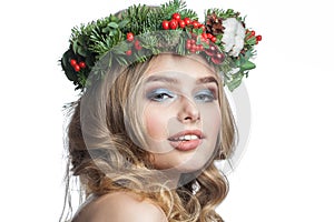 Happy young model woman with wavy blonde hair, makeup and green winter wreath isolated on white background. Beautiful female face
