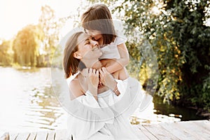 Happy young mom and child girl are hugging by the lake, pond. Mother and daughter smiling while spending free time